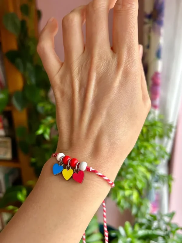 Hand-painted wooden hearts on a red and white cotton Martisor bracelet, representing health, vitality, and prosperity in Romanian culture.